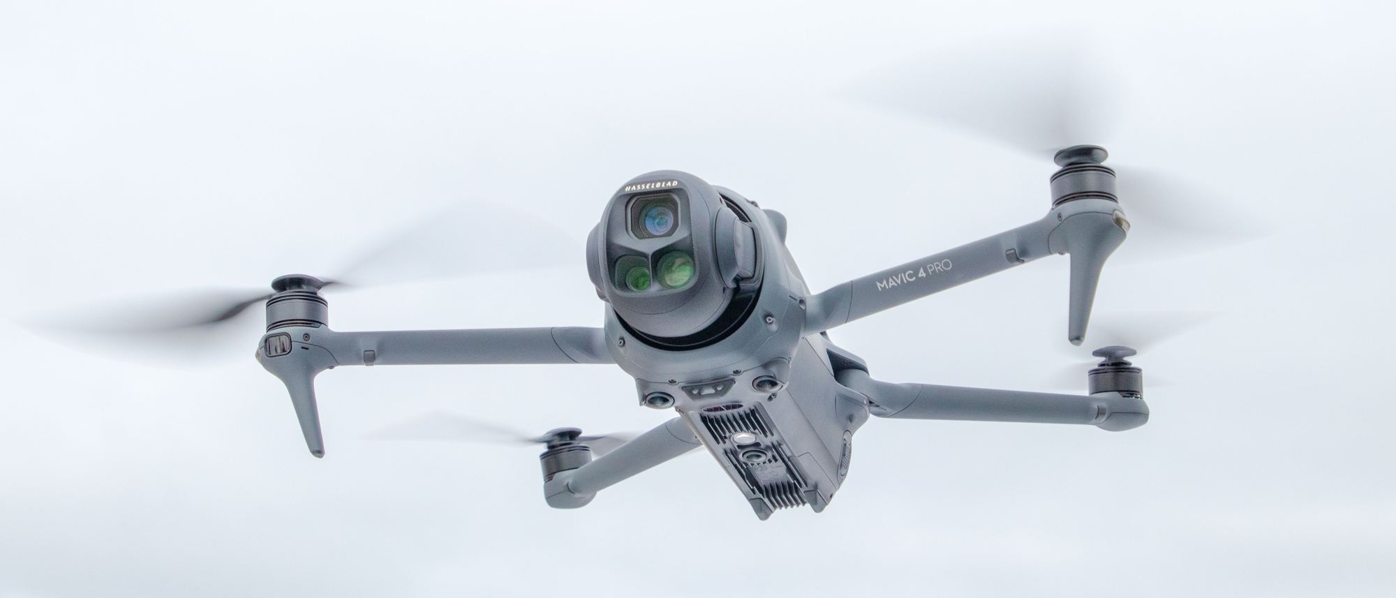 A DJI Mavic 4 Pro hovering head-on against a pale sky
